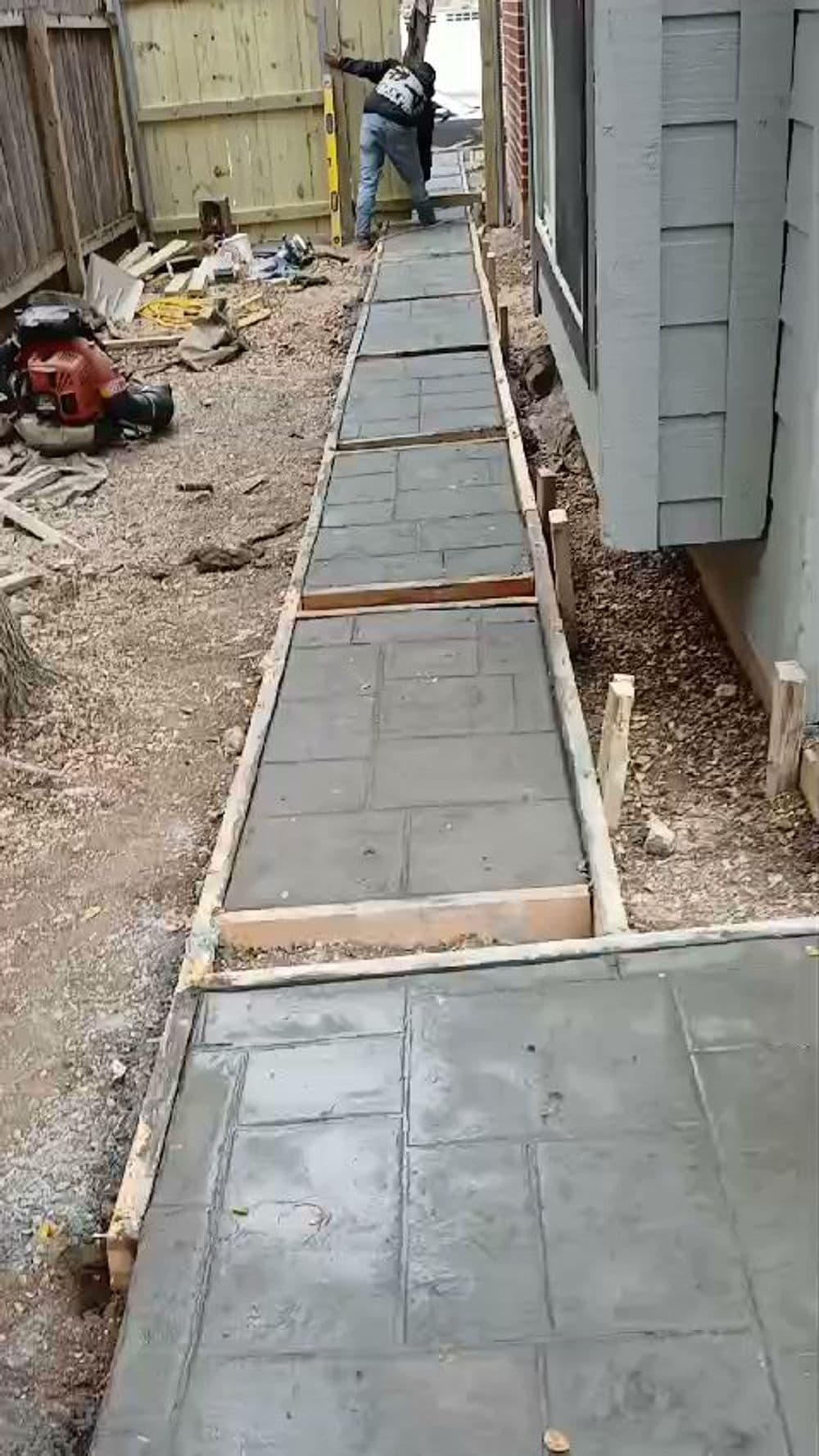 Concrete walkway installation in a residential yard, showing frames and freshly laid pavement.
