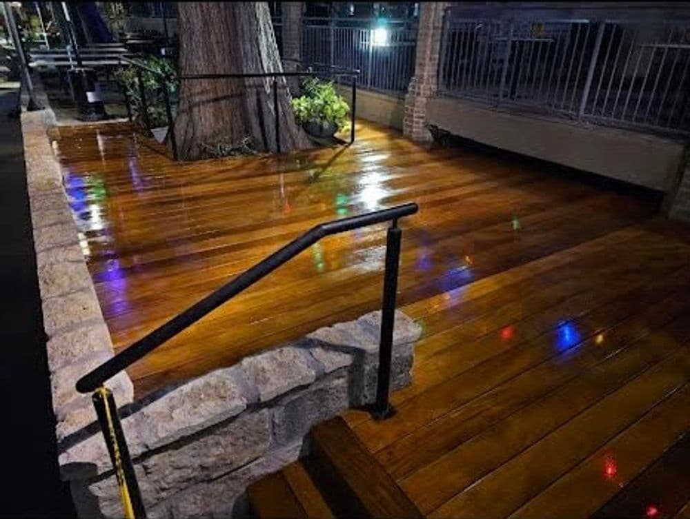 Wooden deck with polished finish, featuring colorful lights and stone railing.