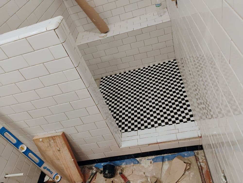 Renovated shower featuring white subway tiles and a black and white checkered tile floor.