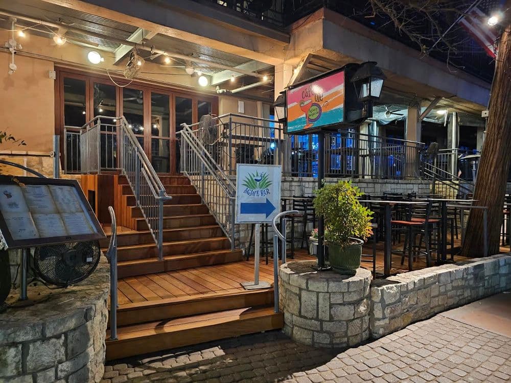 Wooden stairs lead to an outdoor dining area with a vibrant bar and signage for a restaurant.