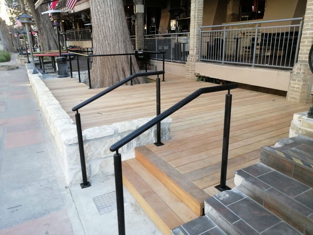 Accessible wooden ramp with black railings next to steps, leading to a restaurant entrance.