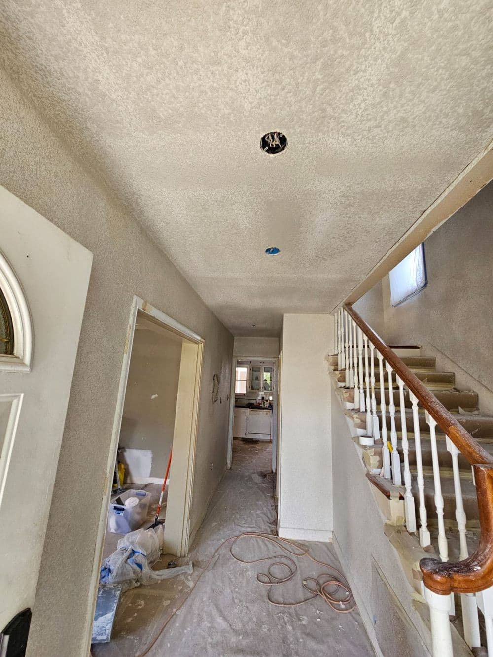Renovated hallway with stairs, drywall, and ceiling fixtures in a home under construction.