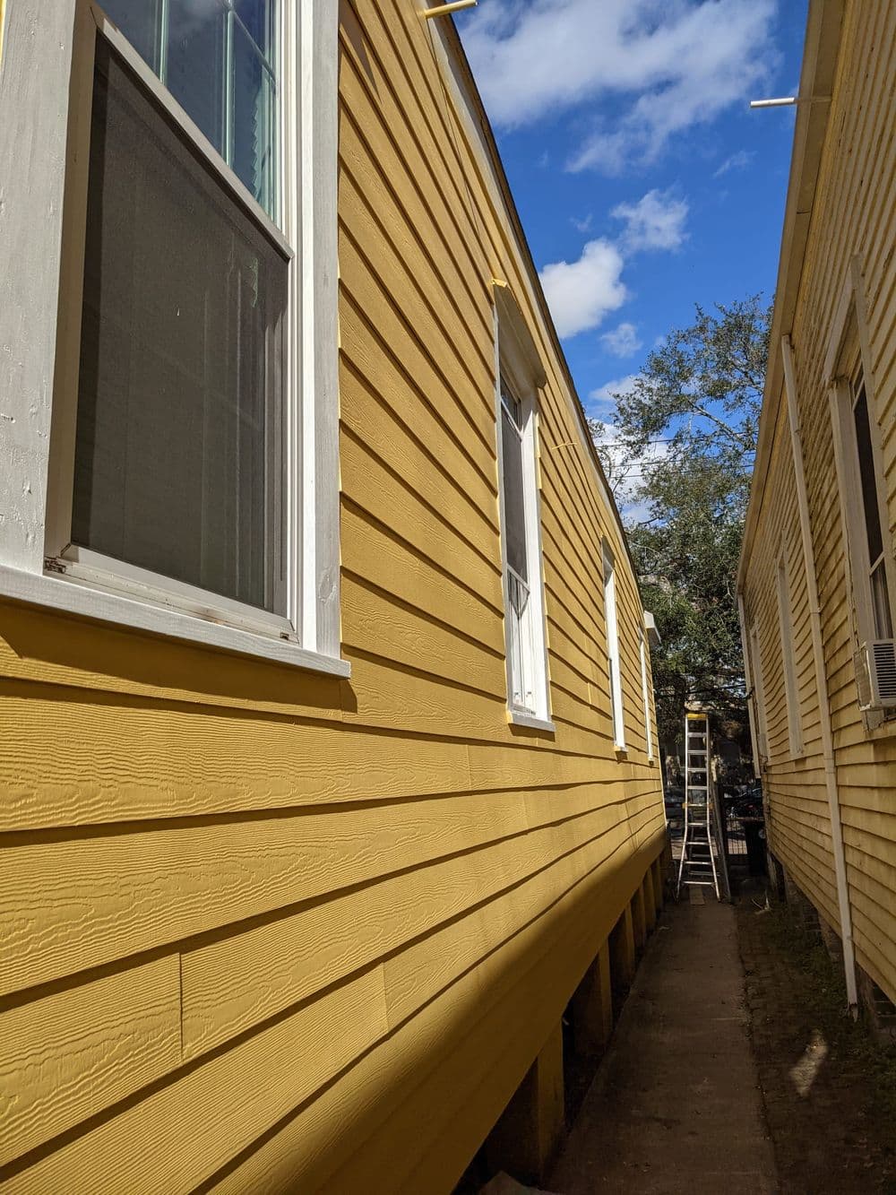 Side view of a yellow house exterior with windows, blue sky, and ladder nearby.