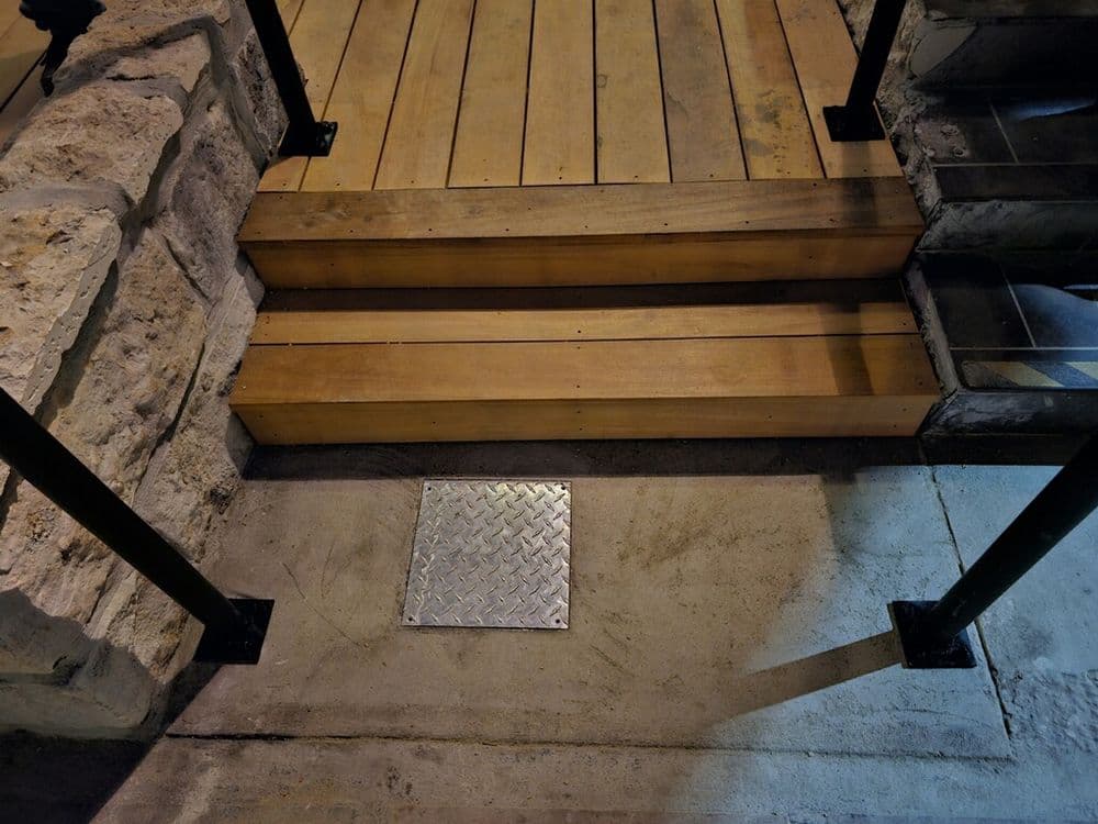 Wooden steps leading to an entrance with metal railing and a diamond plate cover.