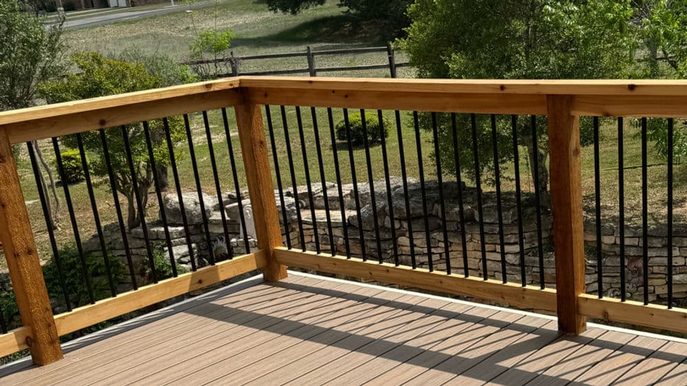 Wooden deck railing with black metal spindles overlooking a landscaped yard.