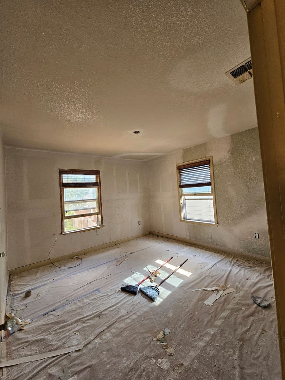 Empty room with unfinished walls and sunlight through windows, covered in construction debris.
