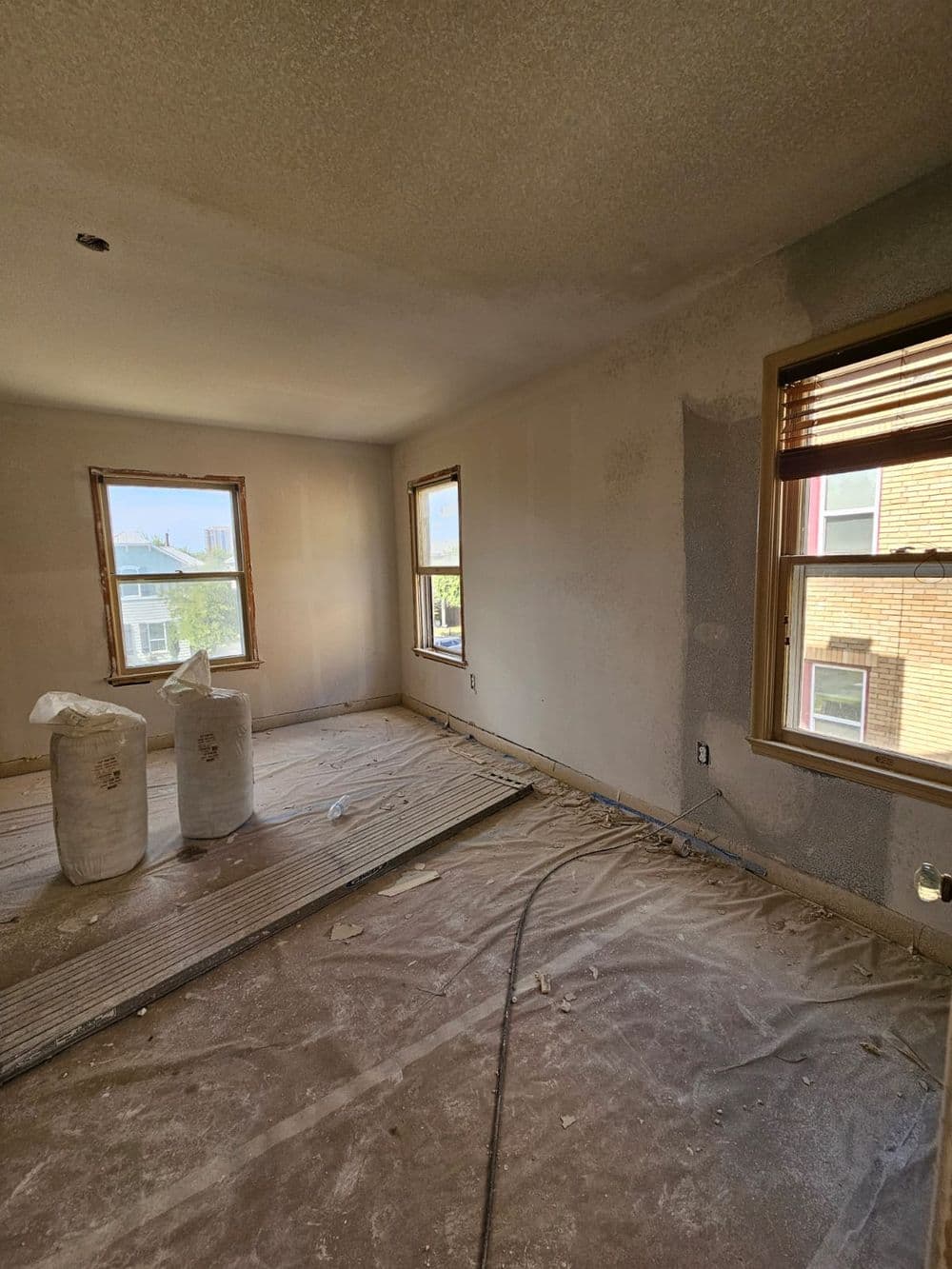 Renovated room with unfinished walls, two bags of plaster, and large windows.
