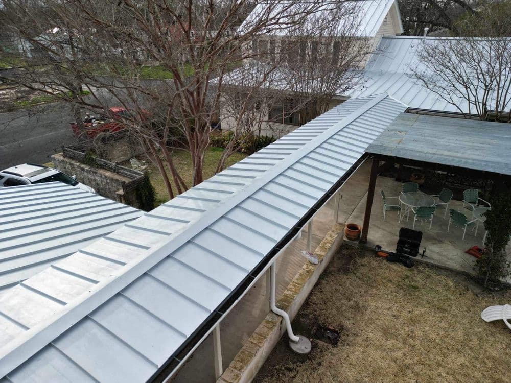 Aerial view of a metal roof with trees and a patio area in a residential setting.