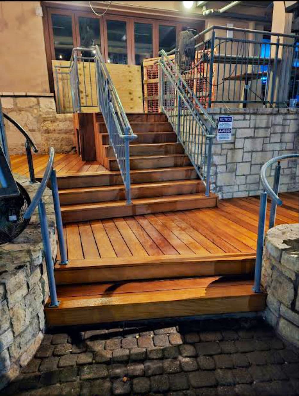 Wooden stairs with metal railings leading to a building entrance, surrounded by stonework.