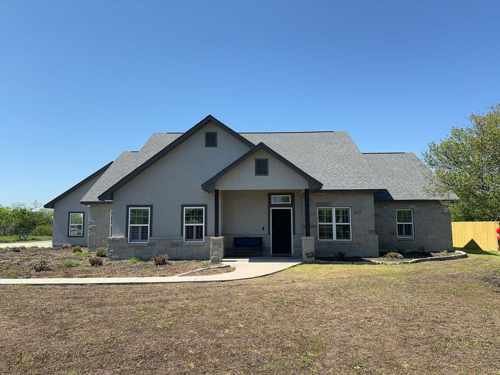 Single-story modern home with gray exterior, large windows, and a landscaped front yard.