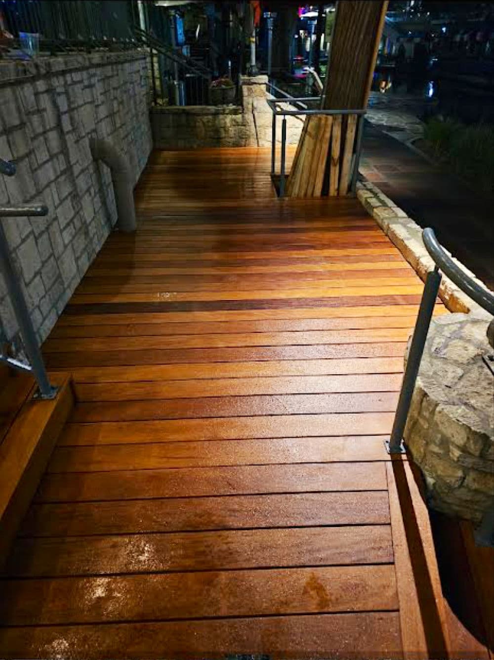 Wooden deck pathway with sleek railings, featuring wet planks in an urban setting.