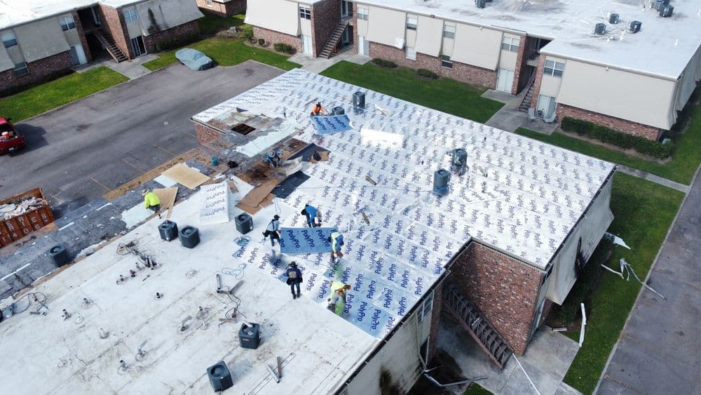 Roofing crew installing insulation and roofing material on a residential building.