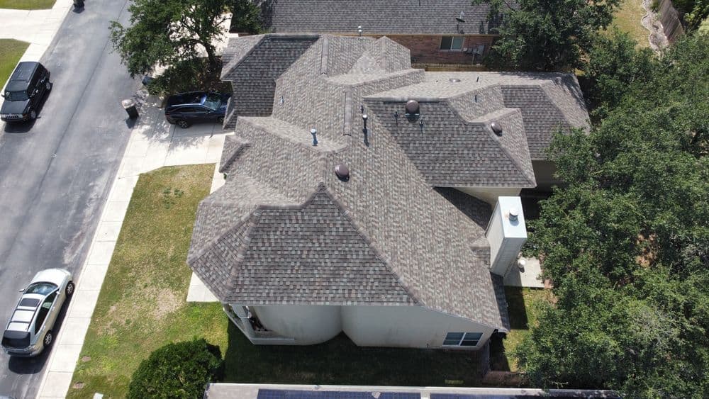 Aerial view of a residential home with a complex roof design and surrounding greenery.