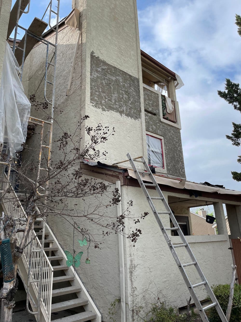 Exterior of a building under renovation with scaffolding and ladders, cloudy sky background.