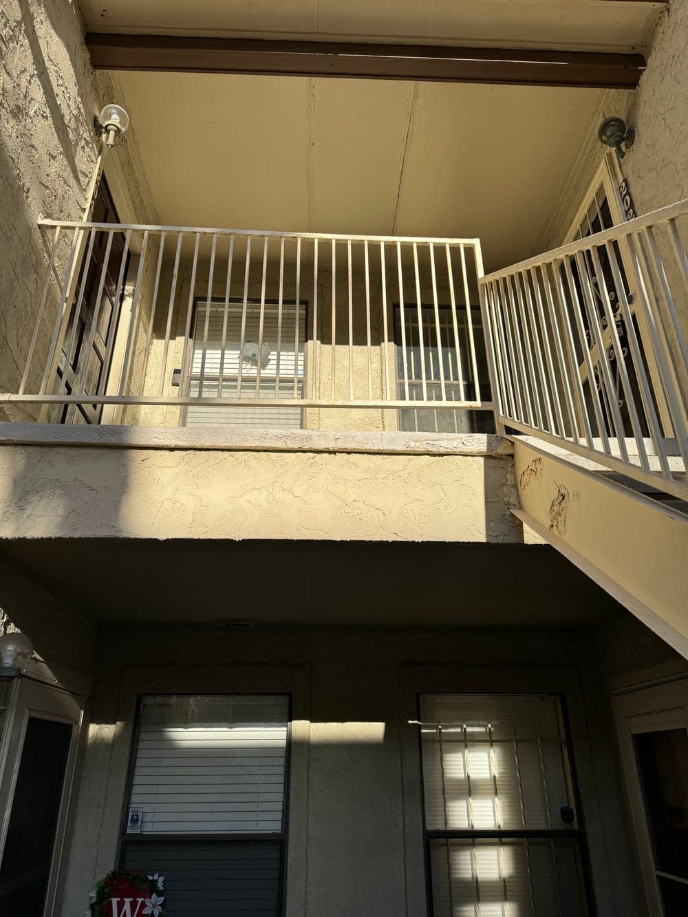 Exterior view of an apartment balcony with railing and sunlight casting shadows.