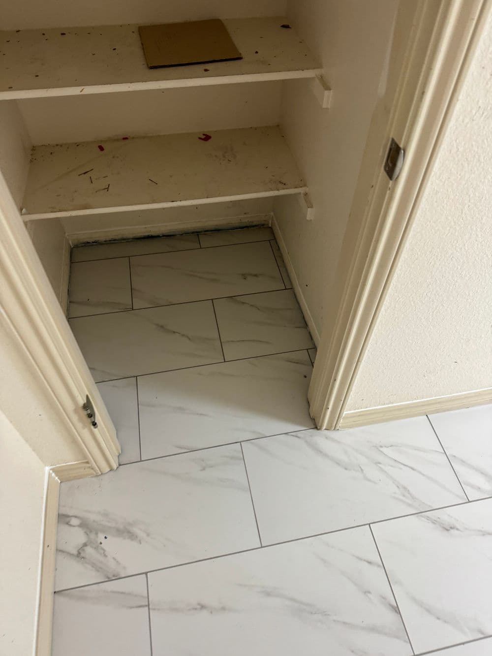 Empty closet with white marble tile floor and shelves, showcasing clean, minimalist design.