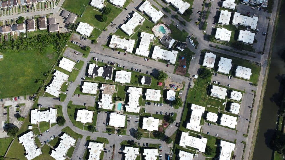 Aerial view of a residential complex with white buildings, green areas, and a swimming pool.