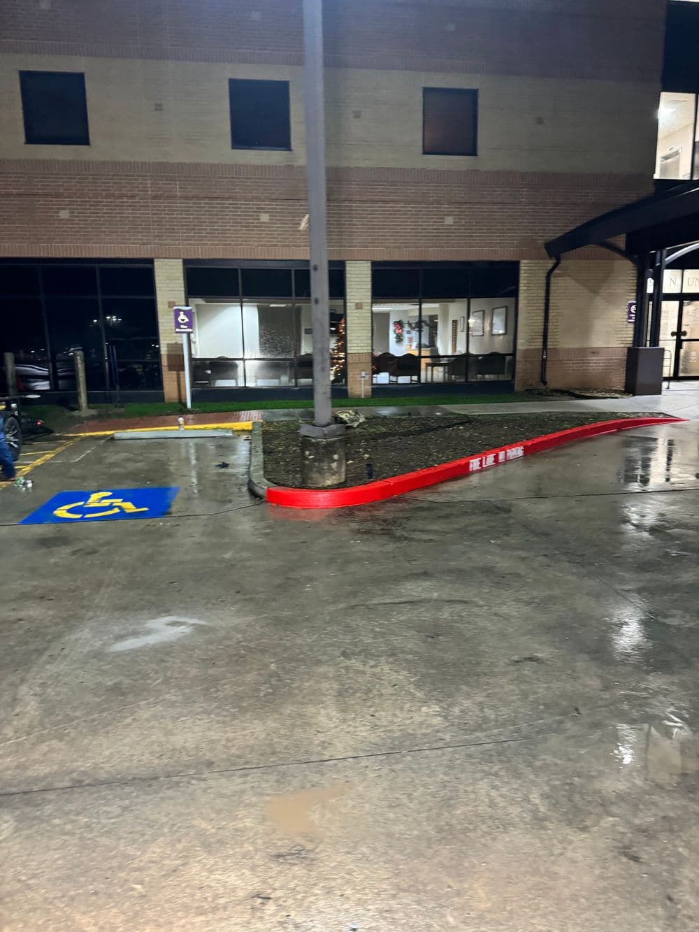 Accessible parking area with wet pavement and building entrance at night.