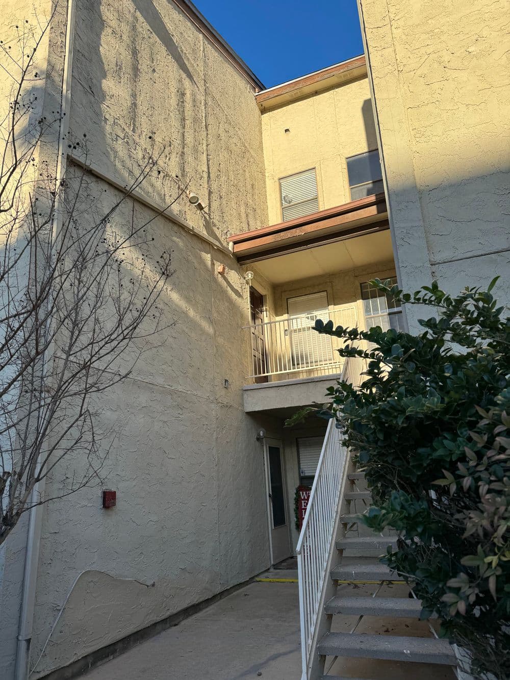 Apartment building corner with stairway, balcony, and textured beige exterior.