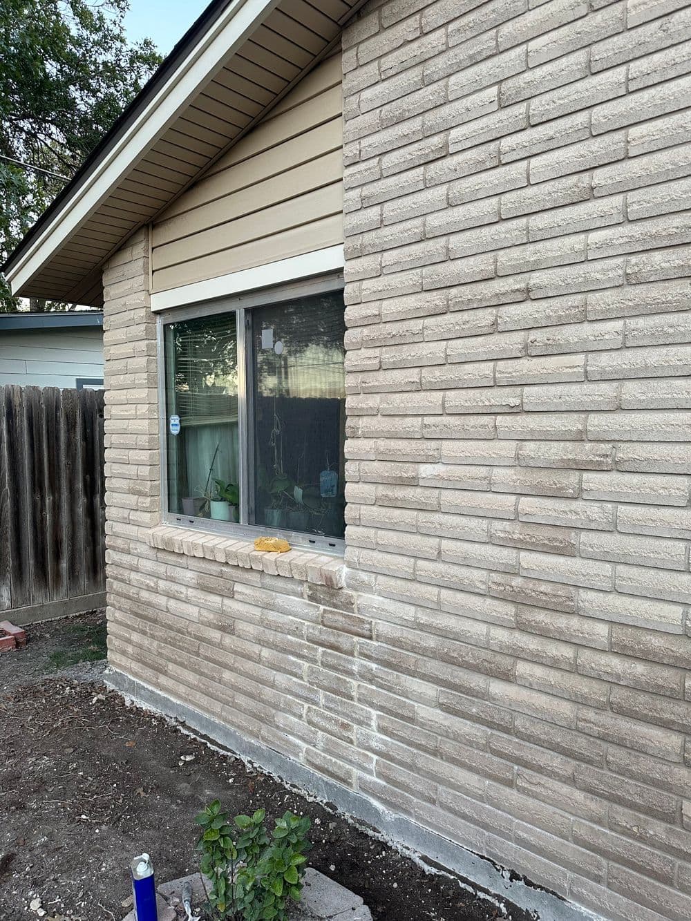 Exterior view of a house featuring textured brick wall and window with wooden siding.