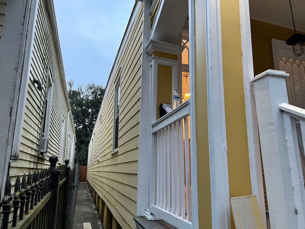 Narrow alley between two yellow houses with a porch and warm interior light visible.