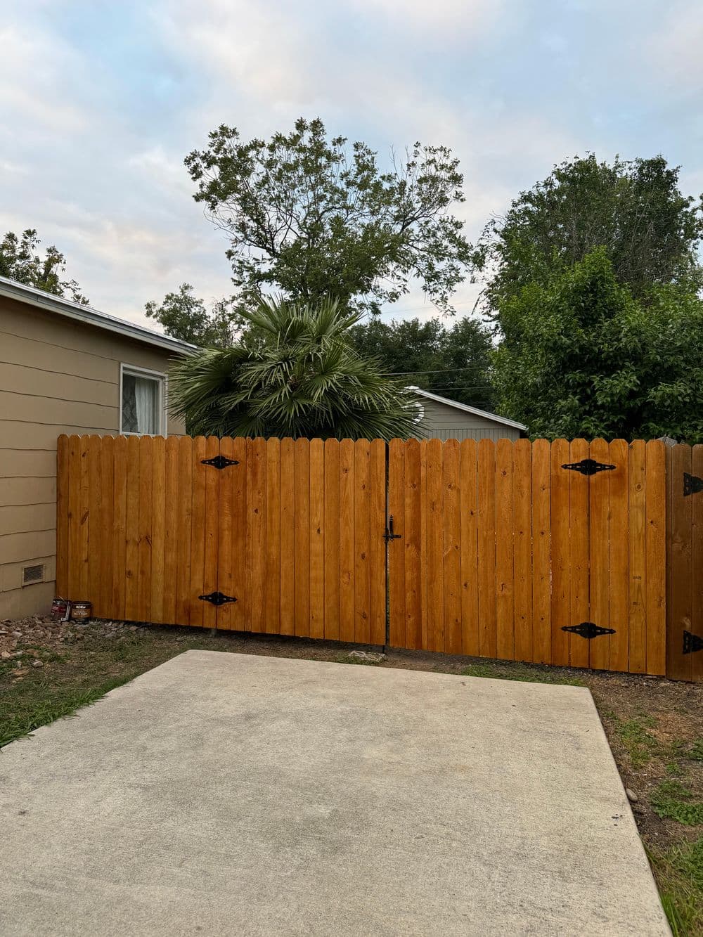 Wooden gate entrance with decorative hinges, surrounded by greenery and palm trees.