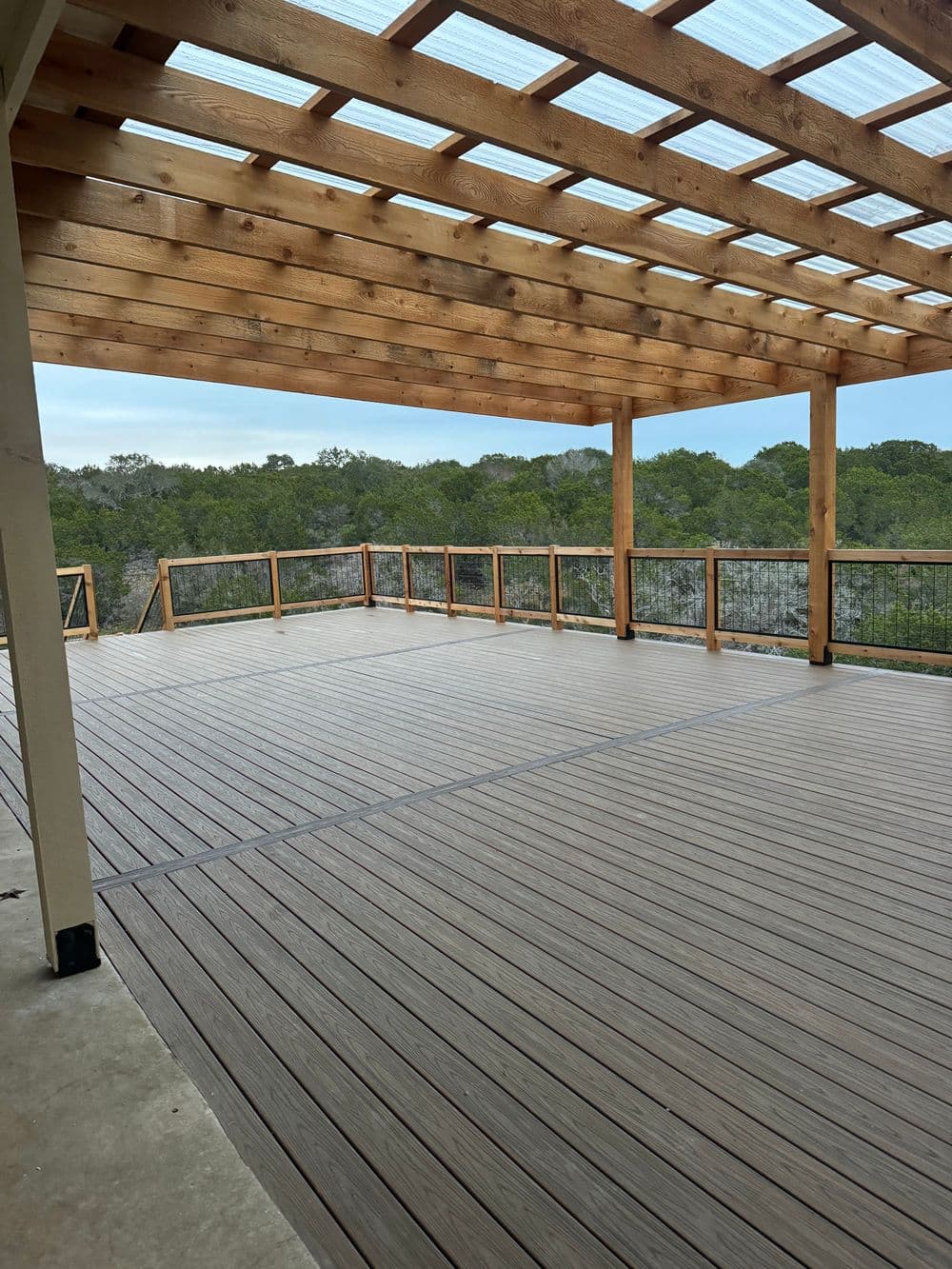 Spacious wooden deck with a pergola and scenic green landscape view.