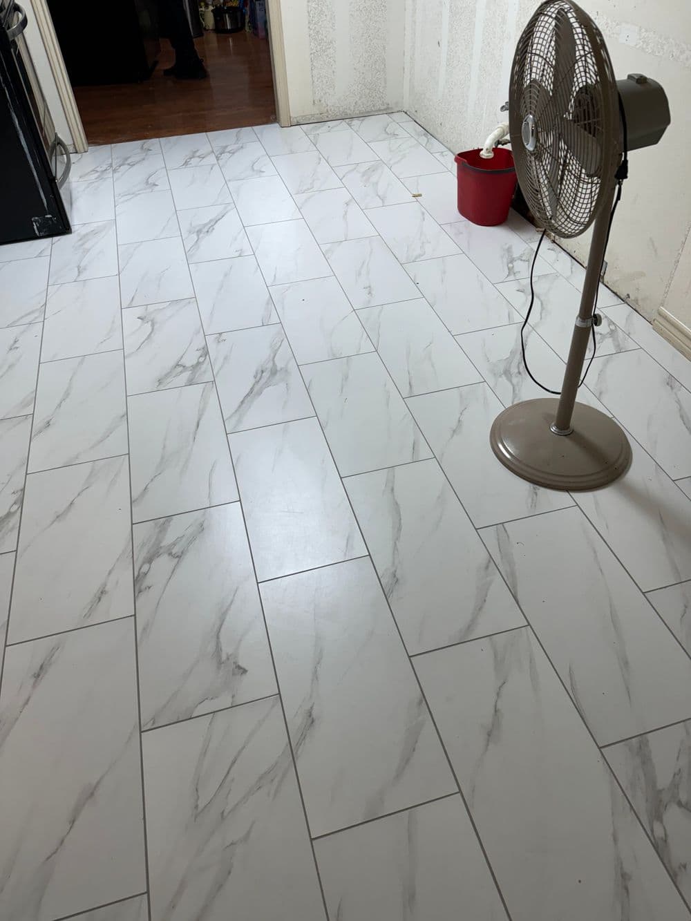 White marble-patterned tile flooring with a standing fan and red bucket in the corner.