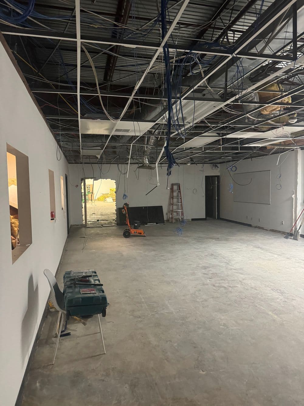 Construction site with exposed wiring and unfinished walls, featuring a ladder and tools.