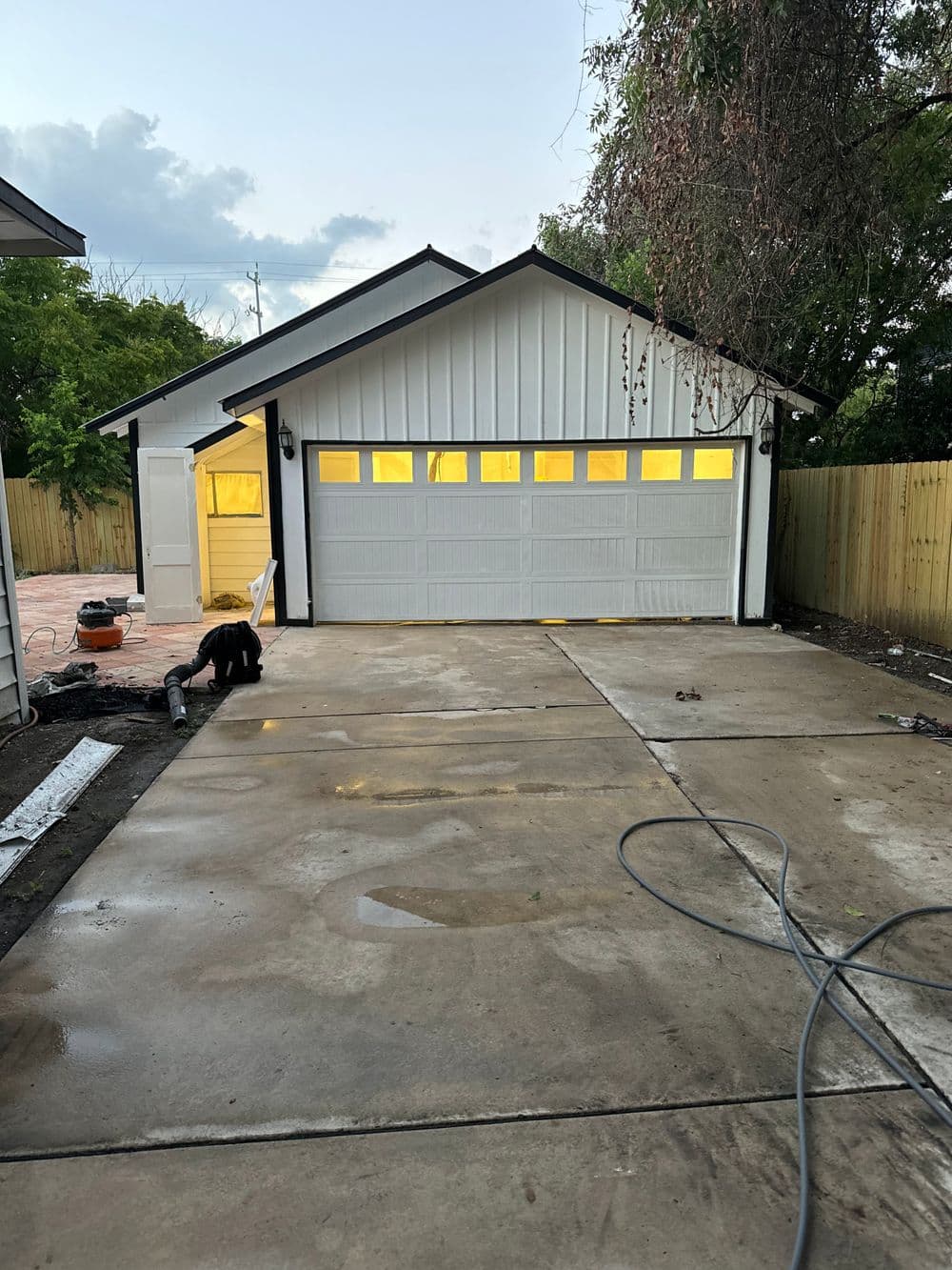 Newly constructed garage with a white exterior and large windows, freshly paved driveway in front.