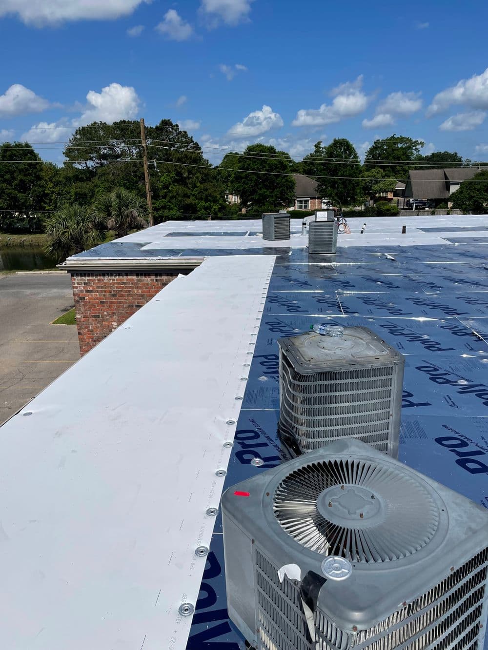 Flat commercial roof installation with HVAC units and blue underlayment in a sunny setting.