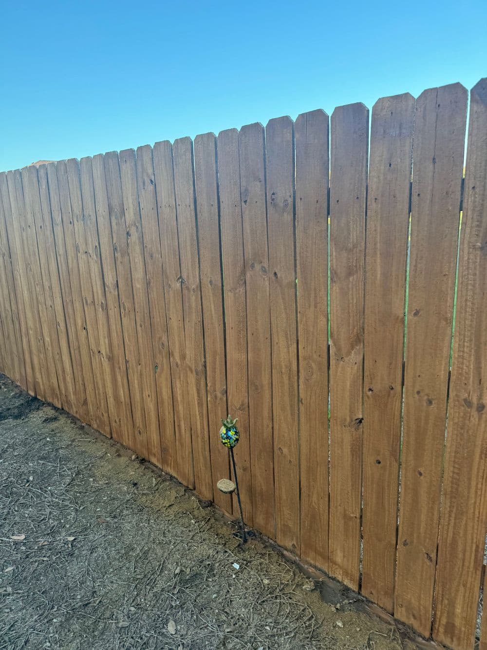Wooden fence with a decorative garden stake and clear blue sky.