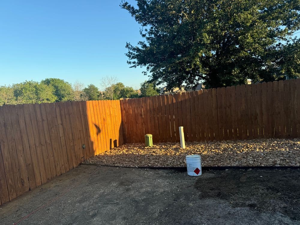 Wooden fence enclosure with gravel base and utility pipes in a sunny outdoor setting.