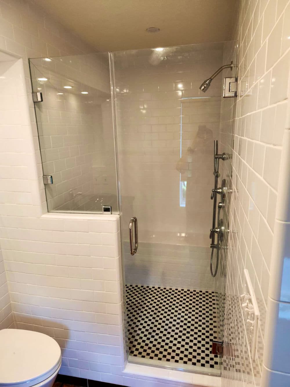 Modern shower with glass enclosure, white tiles, and black and white checkered floor.