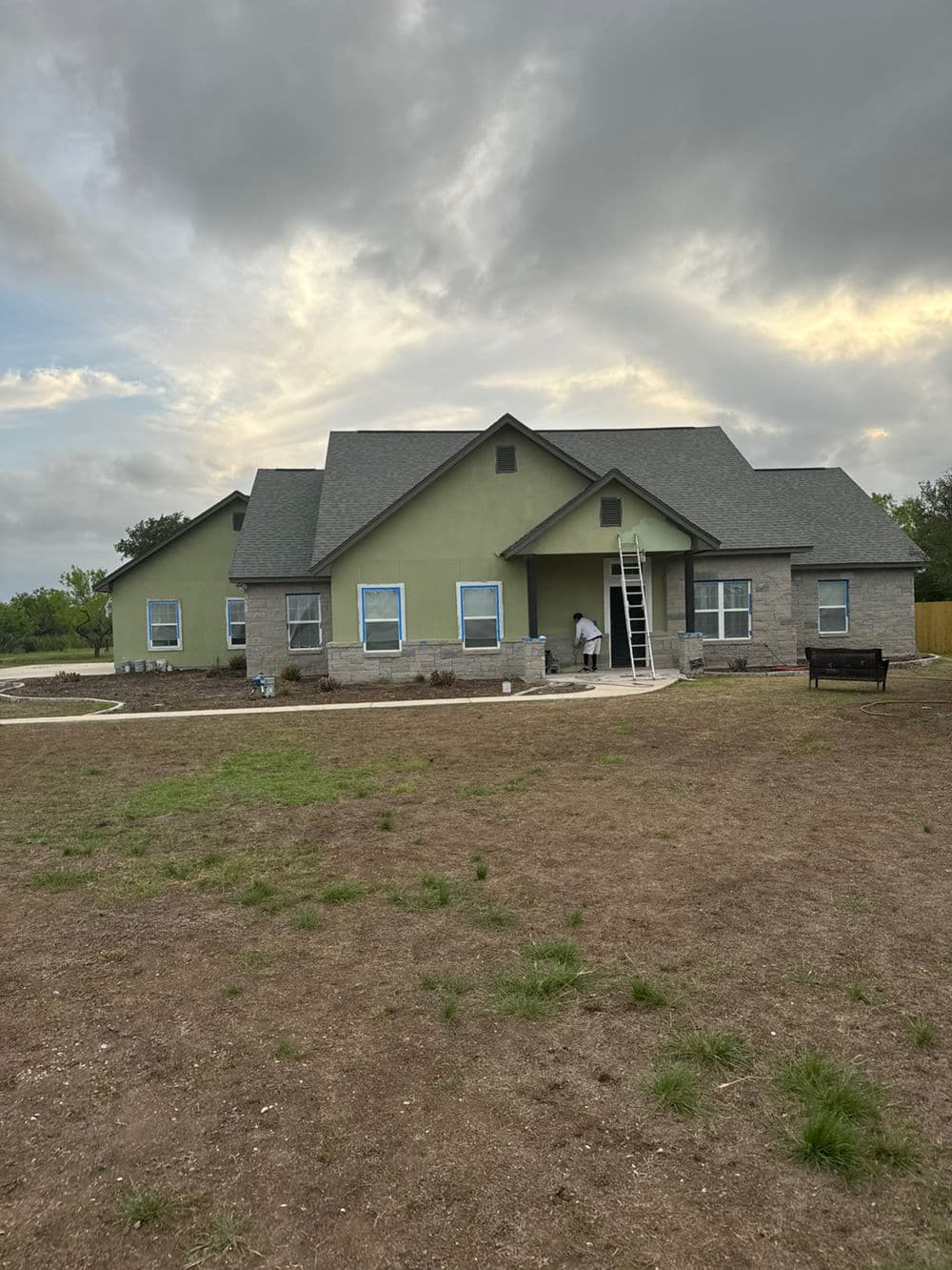 Newly painted modern home with green accents and ladder in front yard under cloudy sky.