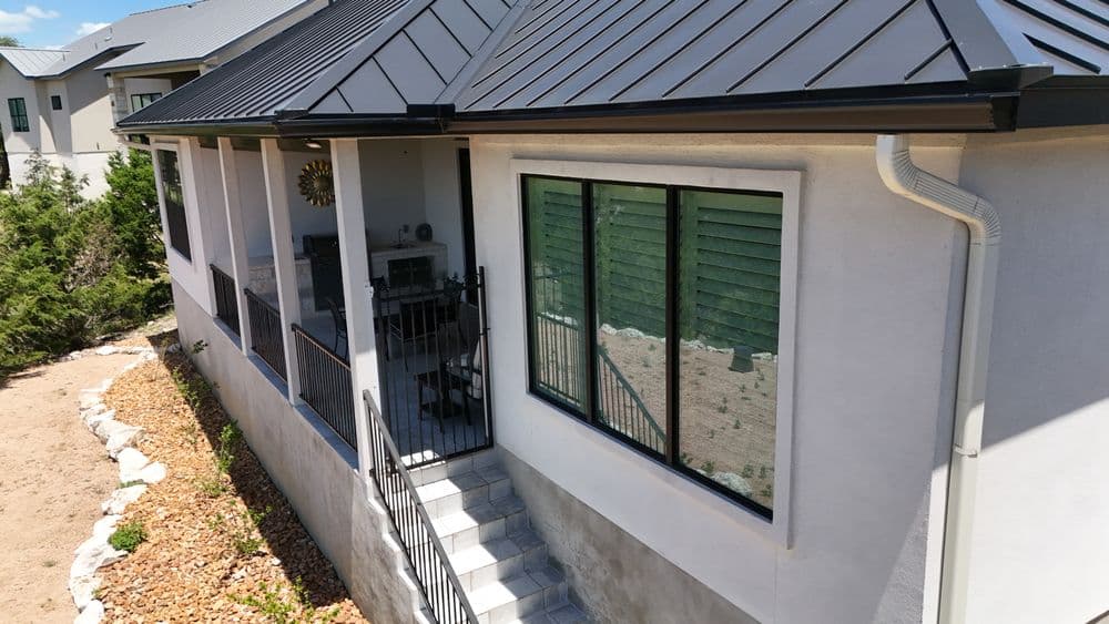 Modern home exterior with black metal roof, large windows, and landscaped yard.
