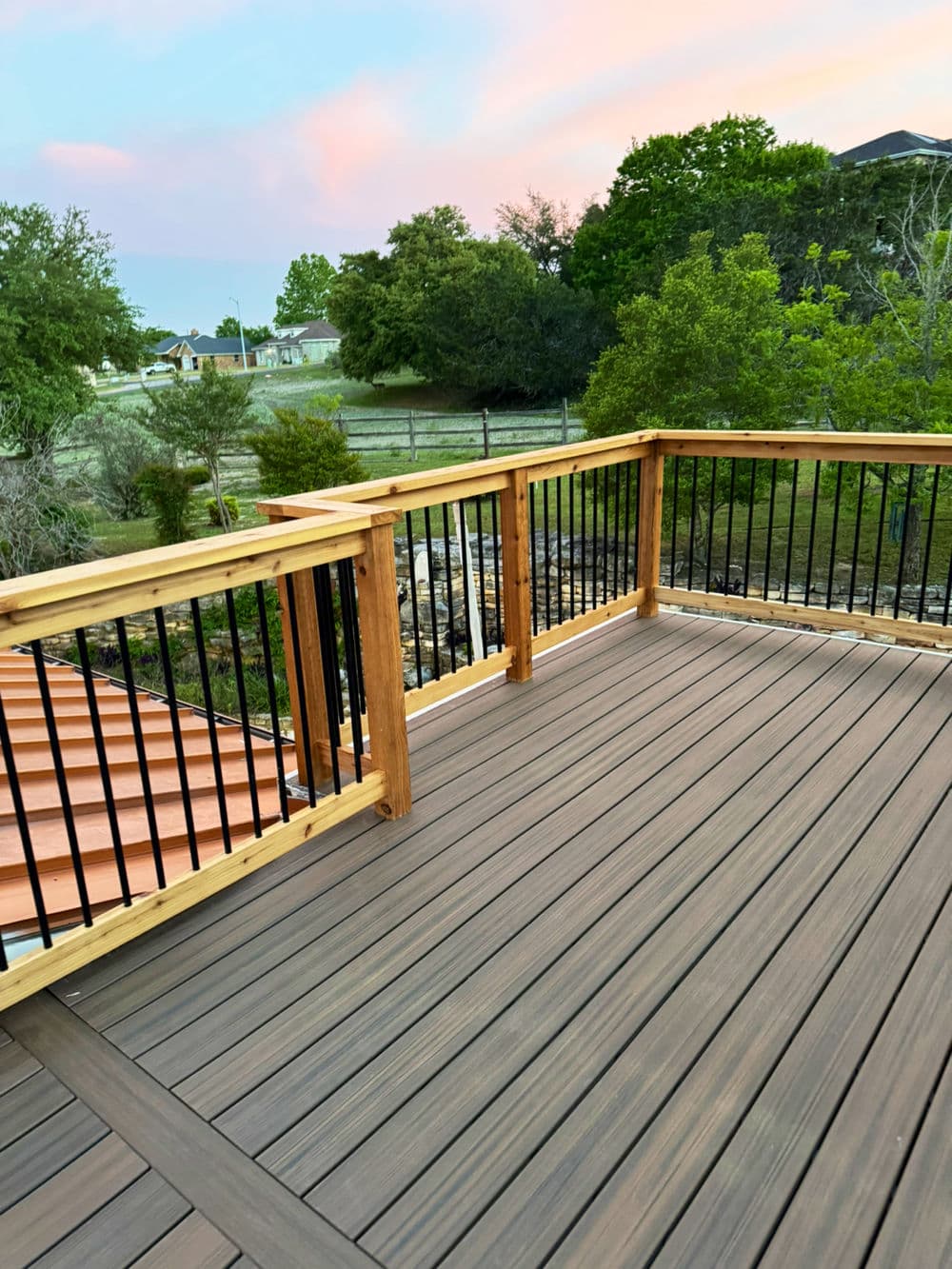 Spacious wooden deck with black railing overlooking a scenic landscape at sunset.