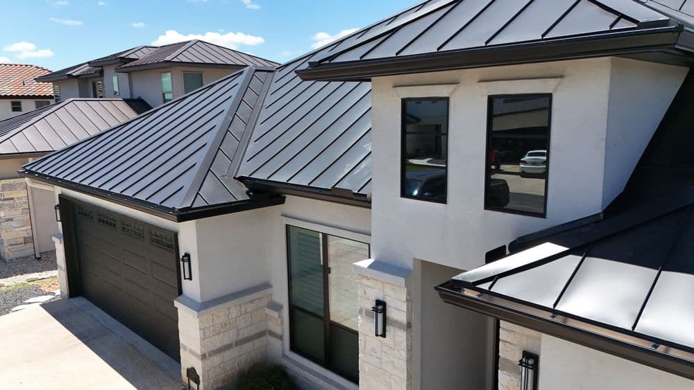 Modern home exterior with metal roof, large windows, and stone accents on a sunny day.
