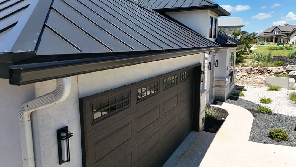 Modern home exterior with black metal roof and stylish garage door in a landscaped setting.